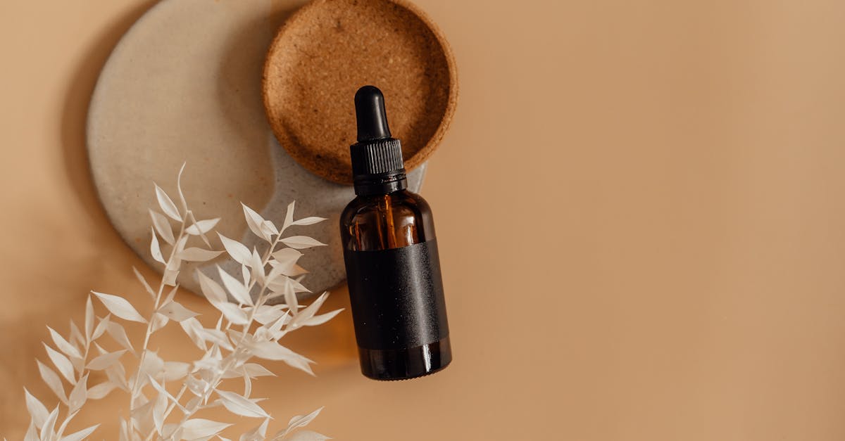 A minimalist skincare bottle with a dropper in a flat lay on a neutral background, surrounded by dried leaves.